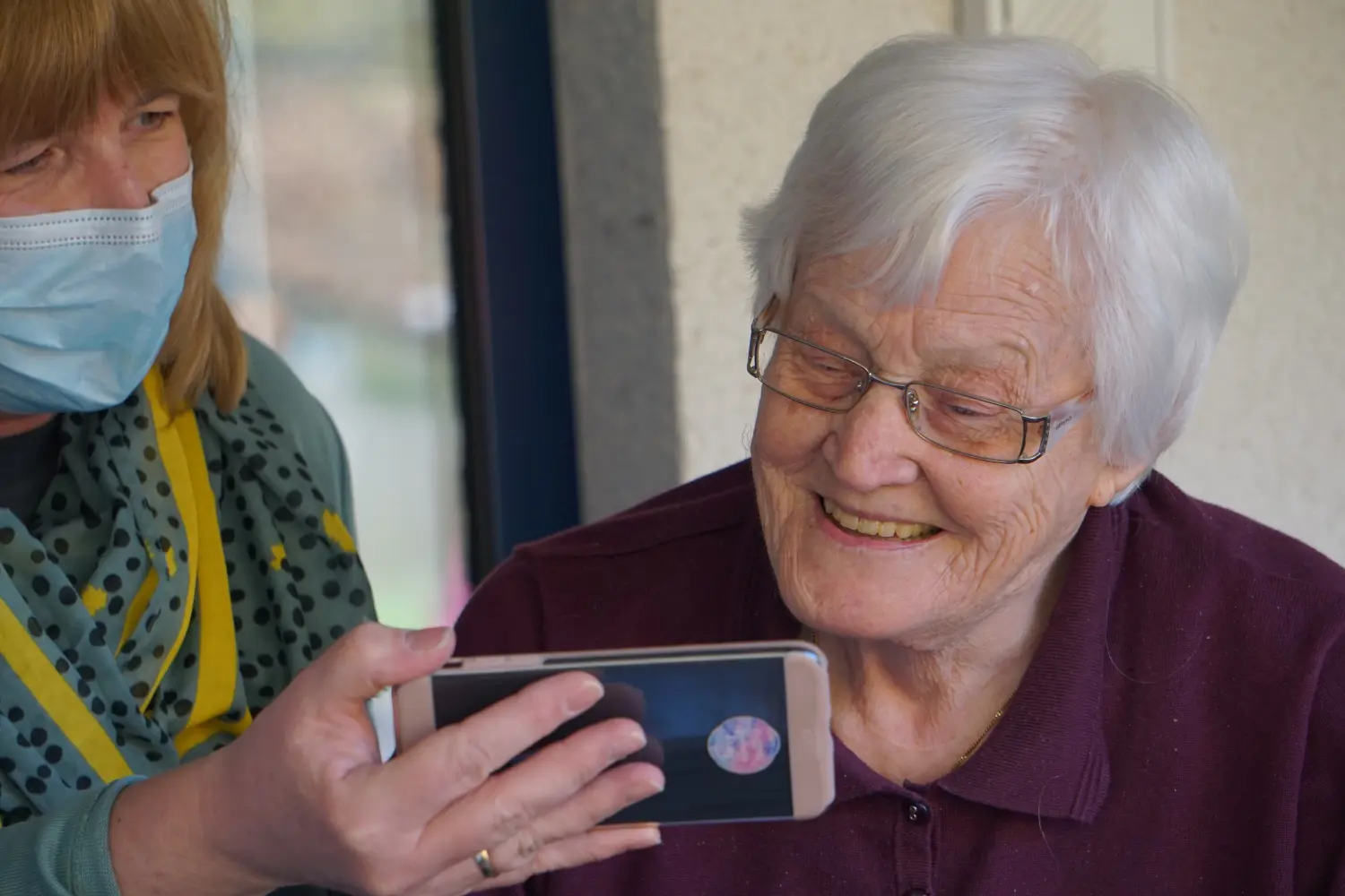 Alte Frau lächelt, während sie auf ein Mobiltelefon schaut